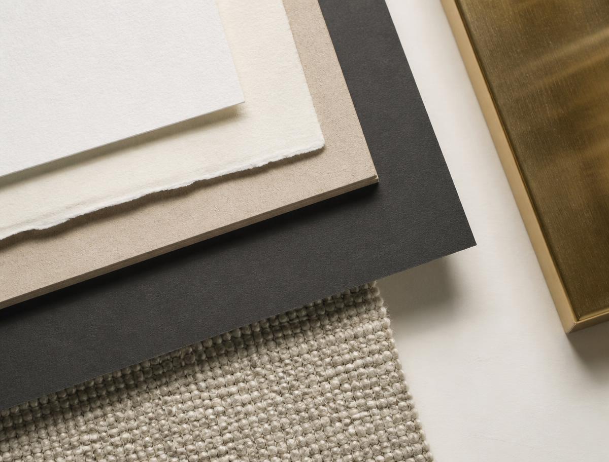 Layered material samples — paper, board, textile and brass — arranged on an ivory surface